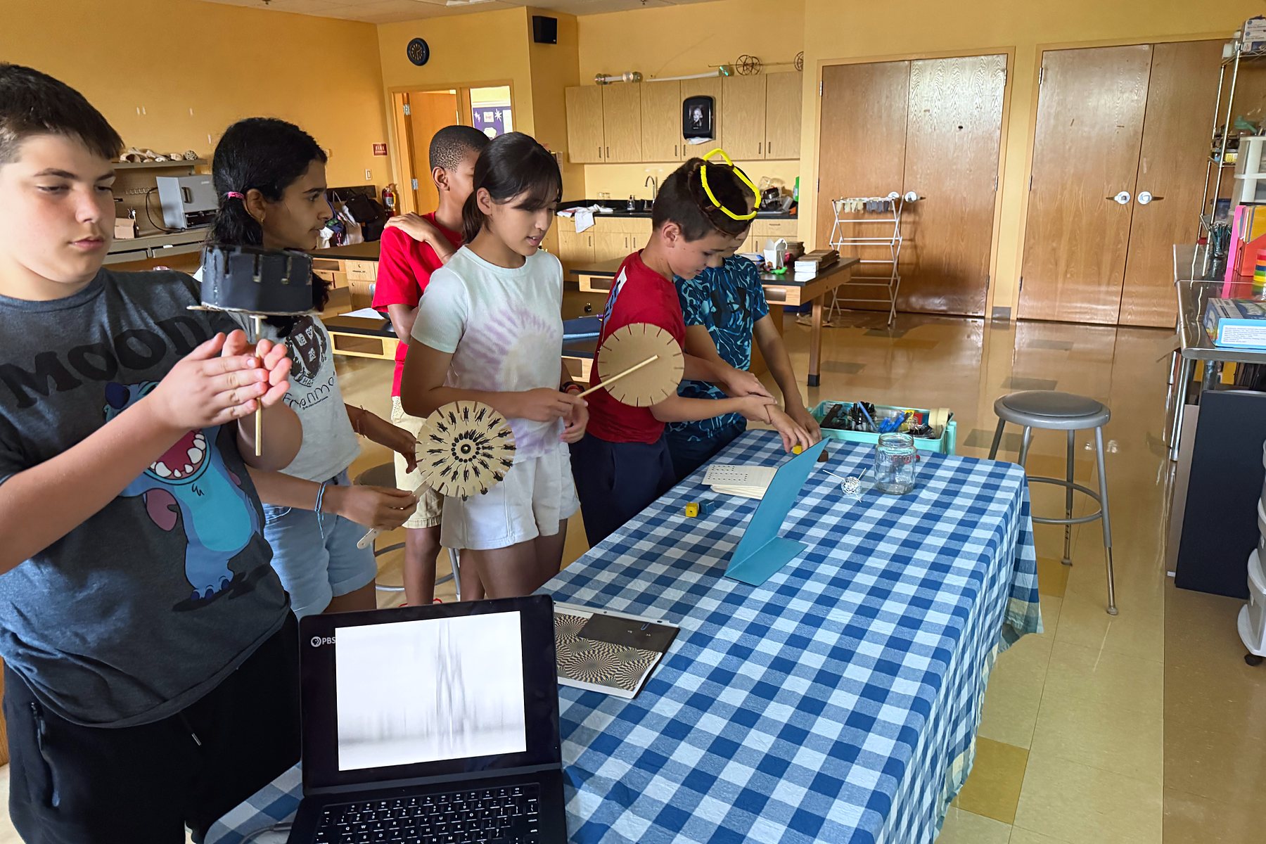 Students spin the optical illusion discs they built at the checkered table, a laptop open beside them